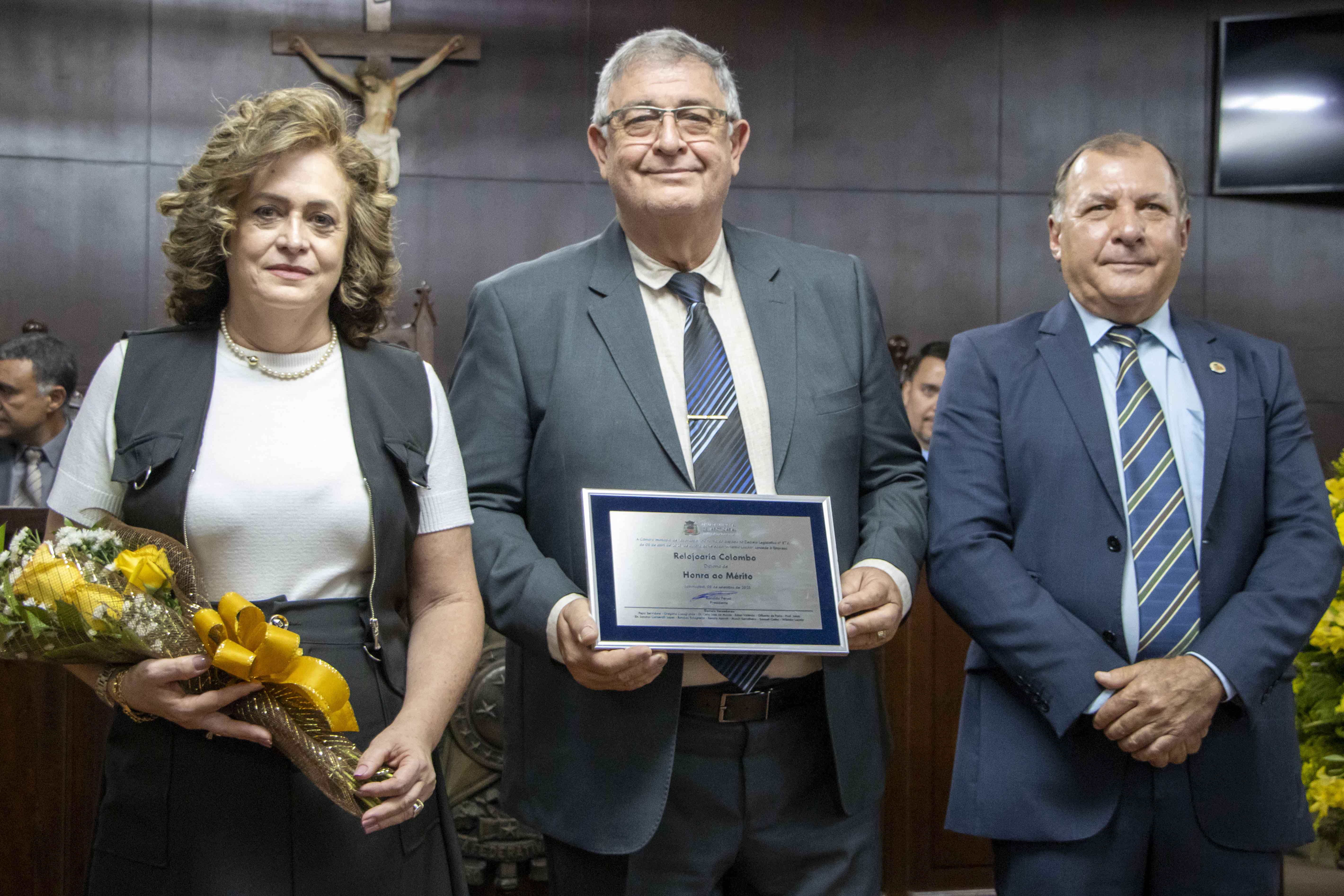 Representantes da Relojoaria Colombo, Márcia Berlingeri e Marcos Alberto, recebem o Diploma de Honra ao Mérito das mãos do vereador Wilsinho Locutor em sessão solene realizada no dia 08/09/2025.